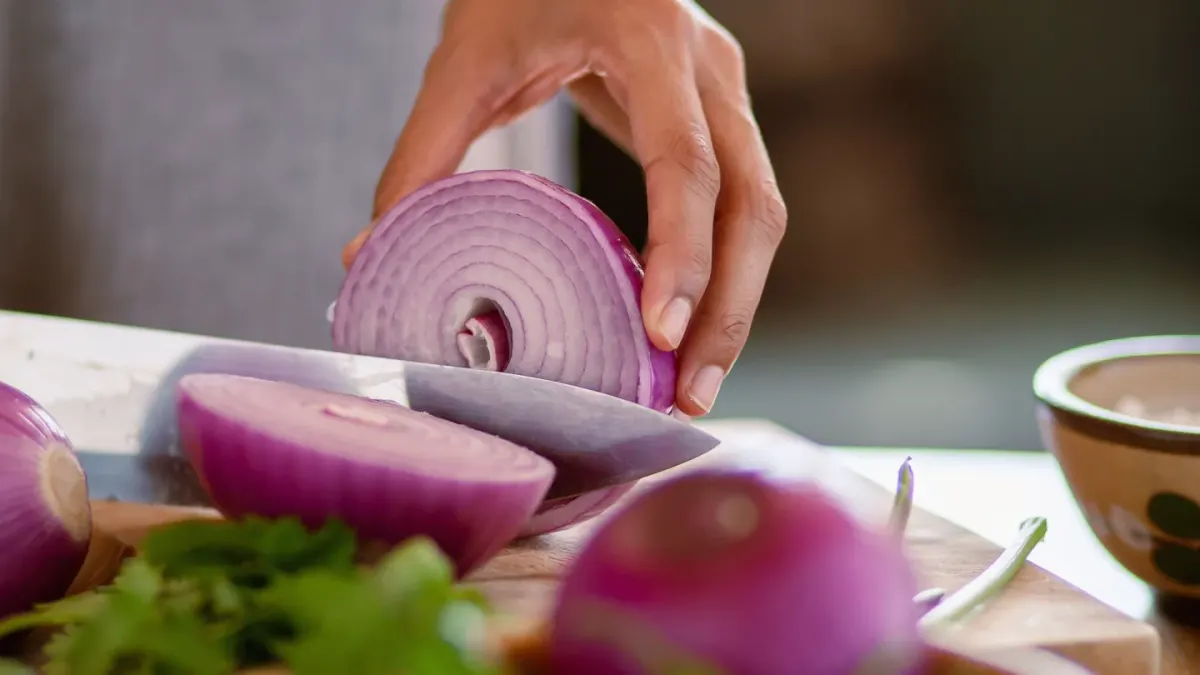 A dog sitting near a kitchen counter where onions are being chopped